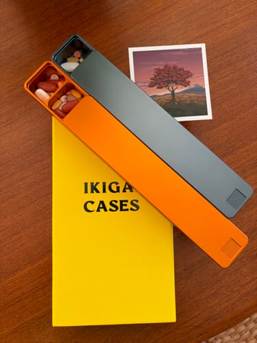 Customer's orange and grey Weekly AM-PM Vitamin Cases open with pills inside, resting on the product box.