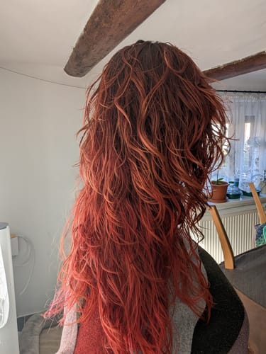 Eine Kundin zeigt ihr langes, rötliches Haar mit definierten Wellen nach der Anwendung der Herbal-Love Haarseife.