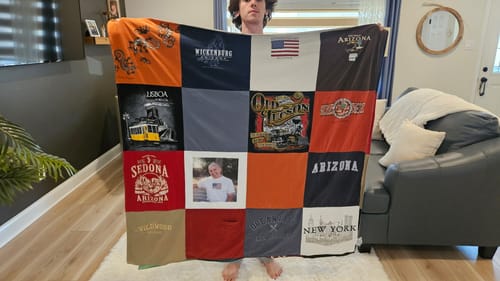 Customer holds up a colorful Project Repat T-Shirt Quilt made from t-shirts, featuring a photo square in the center.