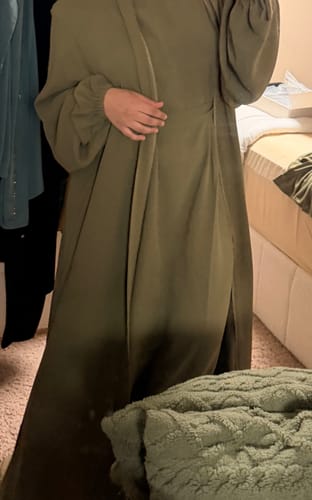 Reviewer wearing a long, green garment with full sleeves and visible cuffs, standing in a bedroom.