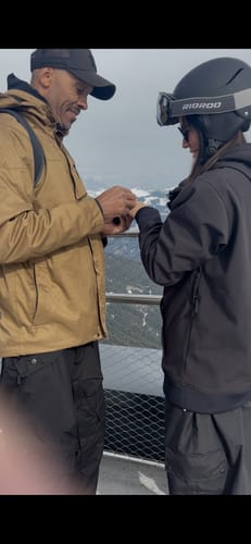 Reviewer wearing the black baggy snow pants on a mountain overlook with another person.