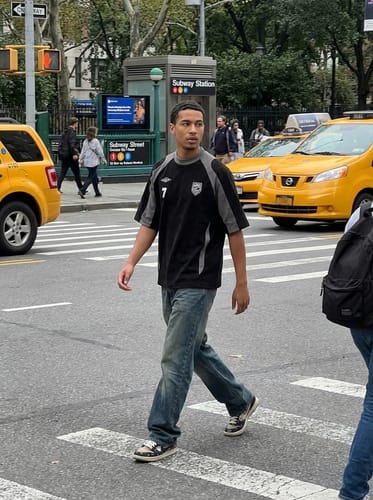 Customer wearing the black Suede-Touch Embroidered Sport T-Shirt with jeans while walking on a city street.