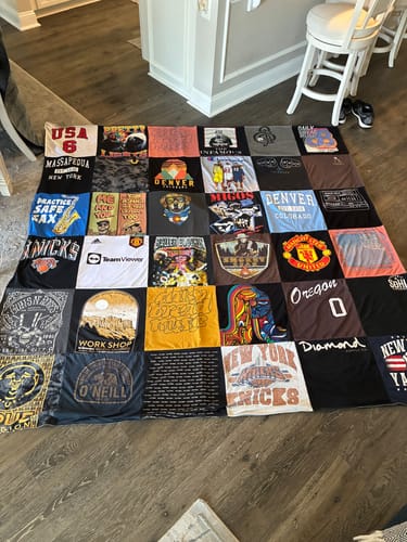 Customer's large Project Repat T-Shirt Quilt made from various shirts, spread out on a wooden floor.
