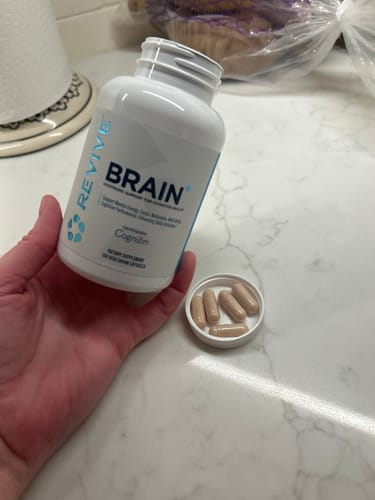 Customer holding an open bottle of Revive Brain+ with the five-capsule serving size shown in the lid.