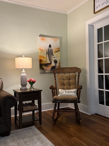 Customer's Parable Of The Lost Sheep Faith Wall Art hung in a living room corner above a wooden rocking chair.