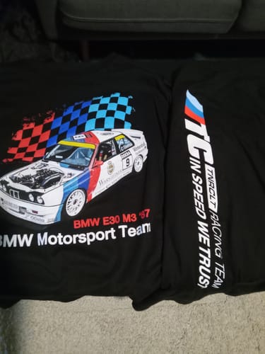 Customer's two black RACING DNA TEEs laid out, showing the front race car graphic and the sleeve's printed logo and text.