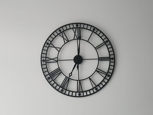 Customer's close-up of the black metal Roman numeral wall clock on a plain white wall.