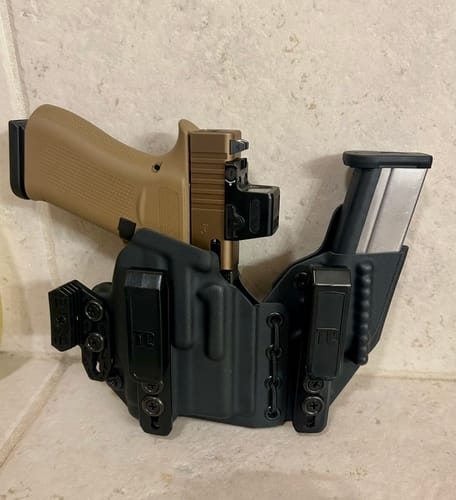 Customer's black AXIS ELITE holster holding a tan handgun and a spare magazine against a tile wall.