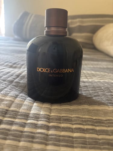 Customer's bottle of Dolce & Gabbana Intenso perfume with a brown cap, sitting on a striped bedspread.