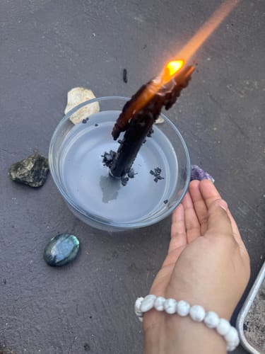 Customer's hand wearing a white beaded crystal bracelet, with a burning candle and other crystals nearby.