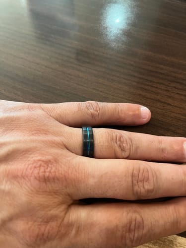 Customer wearing the black Stratus ring, showing the vivid blue groove on their finger against a wood table.