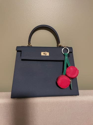 Customer's dark, structured Kally Leather Bag sitting on a beige surface with a red cherry charm attached.
