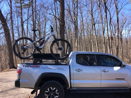 Reviewer's mountain bike mounted on a truck rack, ready for an outdoor ride in the woods.