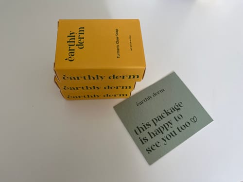 Reviewer shows a stack of three yellow boxes for the Turmeric Fade & Glow Bar on a white surface.