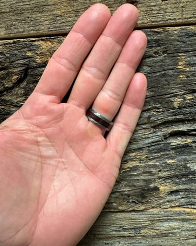 Customer's hand wearing the replacement ring with a dark wood inlay against a rustic wood background.