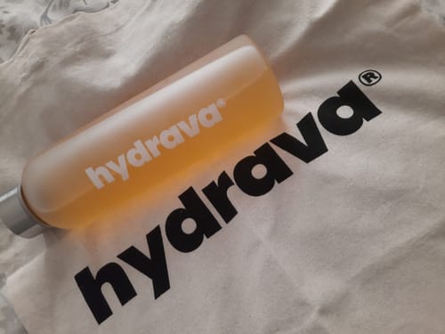 Customer's tote bag with a large black logo, with a frosted water bottle resting on top.