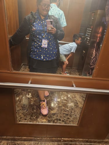 Reviewer taking a mirror selfie wearing the Disney's Tangled "Lanterns" shirt, a black jacket, and pink sneakers.