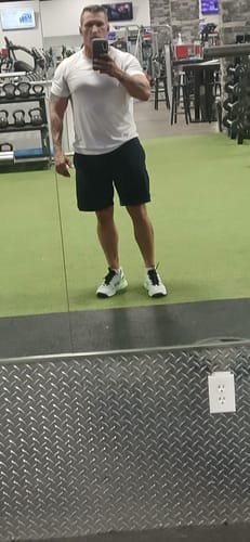 Customer taking a mirror selfie in a gym, showcasing his physique in a white t-shirt before his cycle.