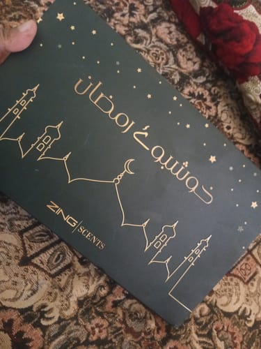 Reviewer holding the elegant, dark green Khushboo-e-Ramzan gift box with gold lettering and mosque outlines.