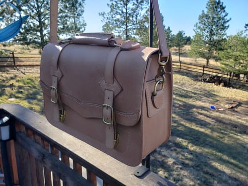 Customer's finished light brown Western Leather Laptop Bag hanging on a deck, showing the side profile and front buckles.