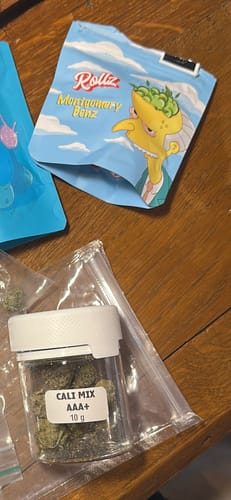 A customer's small, clear jar of CALI MIX AAA+ flower, labeled '10 g', sitting on a wooden table.