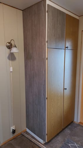 Anmelder viser et skap delvis fornyet med perlegrå kontaktplast, sammenlignet med de originale dørene.