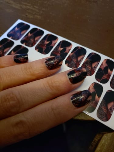 Die Hand einer Rezensentin mit aufgetragenen 'Rose Gold Fury' Nagelfolien, die über dem Bogen mit unbenutzten Folien liegt.