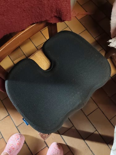Photo d'un client montrant le coussin d'assise orthopédique Cellsius noir posé sur une chaise en bois.