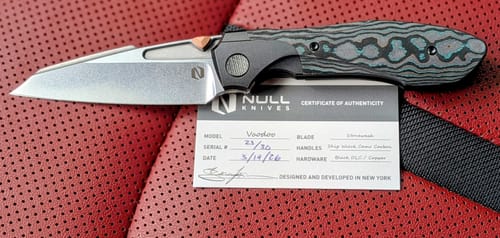 Customer's Null Knives Voodoo knife with a distinctive camo carbon handle and stonewashed blade, next to its authenticity card.