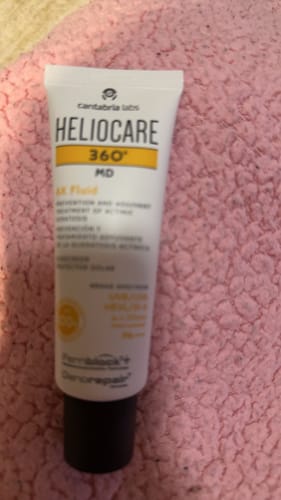 レビュアーのヘリオケア360° MD AK Fluid SPF100⁺。ピンク色の柔らかな布の上に置かれています。