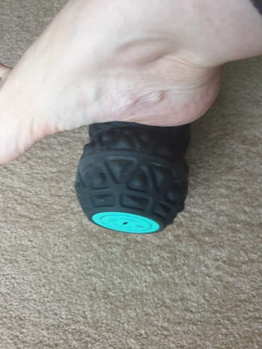 Close-up of a customer massaging the arch of their foot with the black textured Vibit ROLL on a carpet.