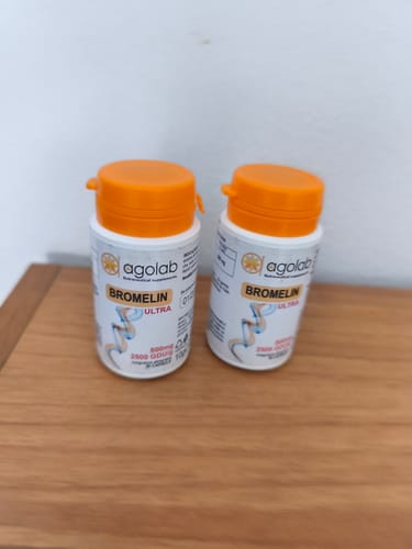 Cliente mostra due flaconi dell'integratore Bromelin Ultra di Agolab con tappo arancione su un tavolo.