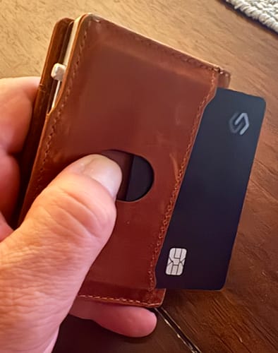 Customer's hand holding a brown wallet with the black SPOTMINDERS Tracking Card PRO in a card slot.