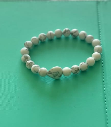 Reviewer's white and grey marbled bead bracelet from the VIP Crystal Club on a teal surface.