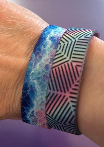 Close-up of a reviewer's wrist wearing the geometric 'We're All Connected' bracelet next to a blue patterned bracelet.