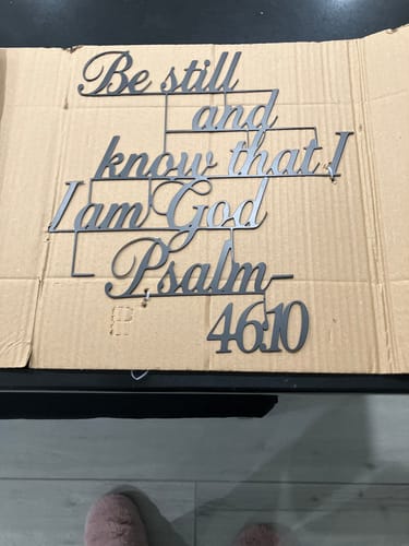 Customer's black metal Psalm 46:10 wall decor unboxed and laid out on a piece of cardboard.