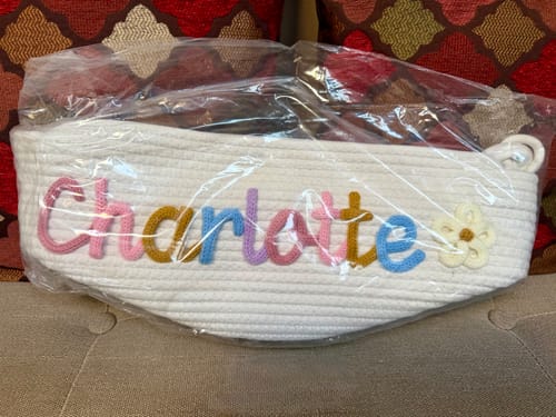 Reviewer's personalized knitted basket with 'Charlotte' in multicolor yarn and a flower icon, still in its original packaging.