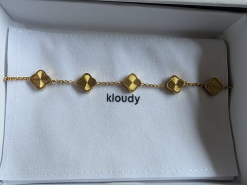 Customer's gold Celine Clover Bracelet with textured clover motifs resting inside its packaging.