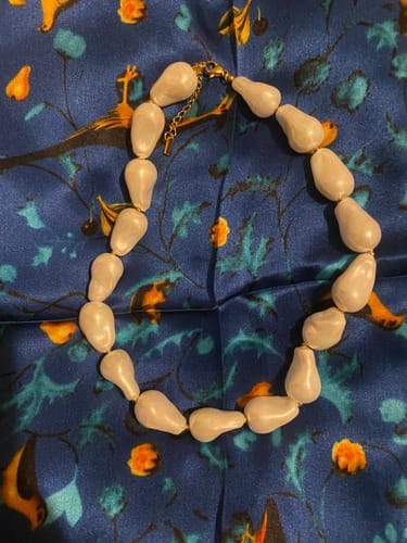 Cliente mostrando el Choker de Perlas con perlas blancas de forma irregular sobre una tela azul.