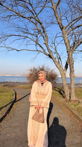 Customer posing outdoors in the light-colored Kaftan Topaz with its wide belt and detailed embroidery.
