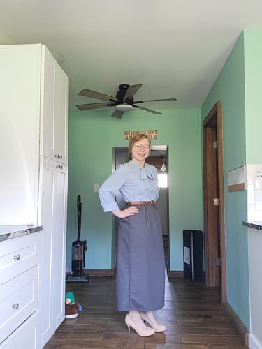 Customer wearing the Blue 1930s Bow Tie Belted Pencil Dress with a brown belt in a hallway.
