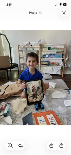 Reviewer's photo of a happy child holding their framed Dino Tamer portrait surrounded by gift wrapping.