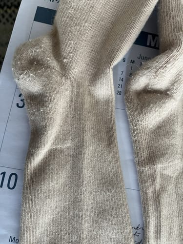 Close-up: Customer's beige compression sock with minor pilling on the heel after washing.