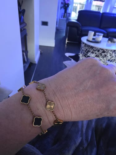 Customer's wrist wearing two Celine Clover Bracelets, one with black enamel clovers and another with textured gold clovers.