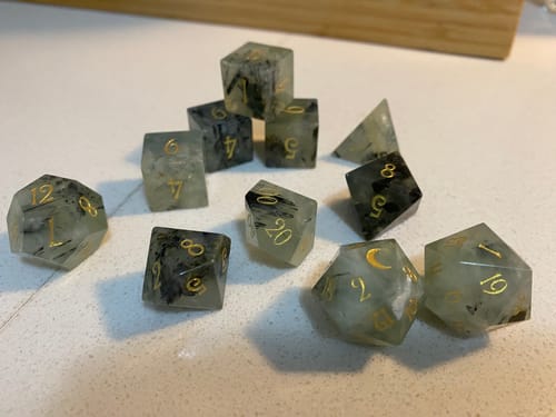 Customer's Prehnite Gemstone Dice Set scattered on a surface, showing the translucent green stone with dark inclusions and gold numbers.