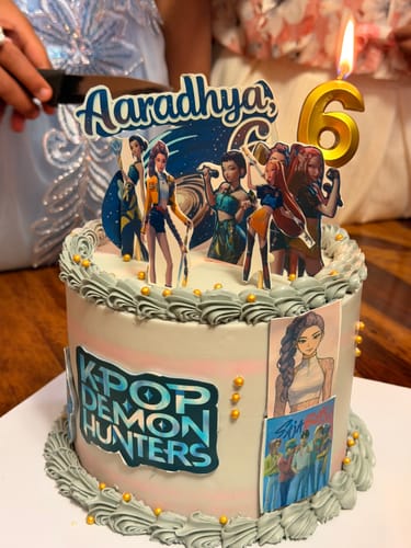 Customer's K-Pop Anime Fusion Cake with character toppers, grey frosting, and a lit number '6' candle.