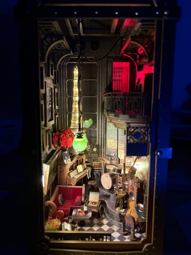 Reviewer's completed Eternal Midnight Paris Book Nook Kit. The detailed miniature jazz club is lit with warm yellow and red lights.