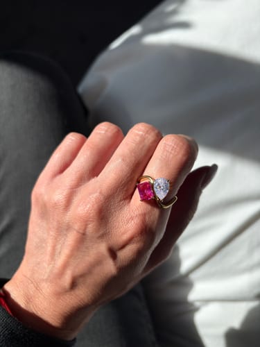 Close-up of a reviewer's hand wearing the Navae Birthstone Ring with a pink radiant-cut and a clear pear-cut stone in the sun.