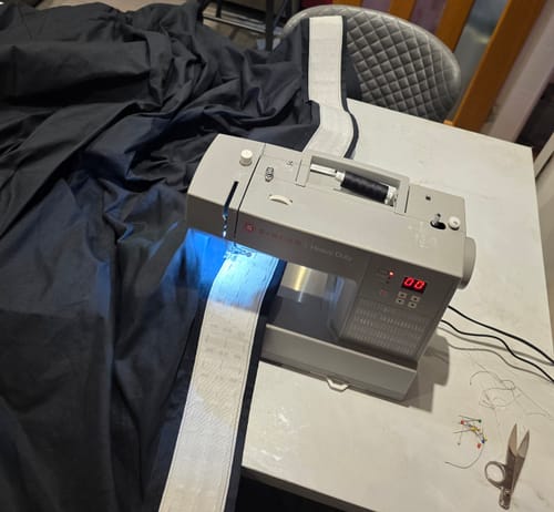 Reviewer's Singer Heavy Duty HD6605 Sewing Machine stitching a thick white header onto large black fabric for a project.