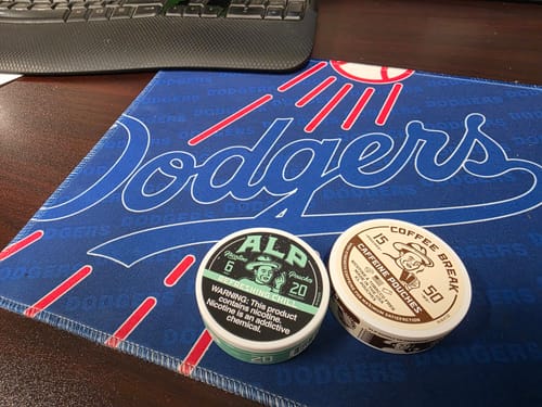 Reviewer's tin of Refreshing Chill Nicotine Pouches next to a tin of caffeine pouches on a desk.